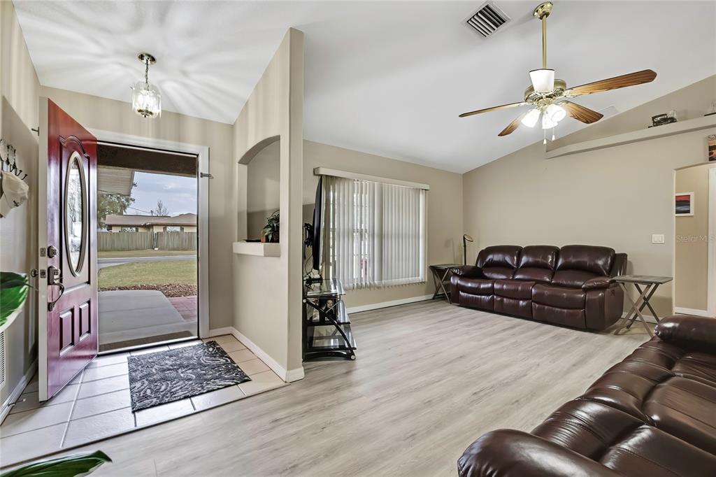 A living room features light wood-look flooring, a ceiling fan, and an open entryway door — 103 DAISY LANE, INVERNESS, FL