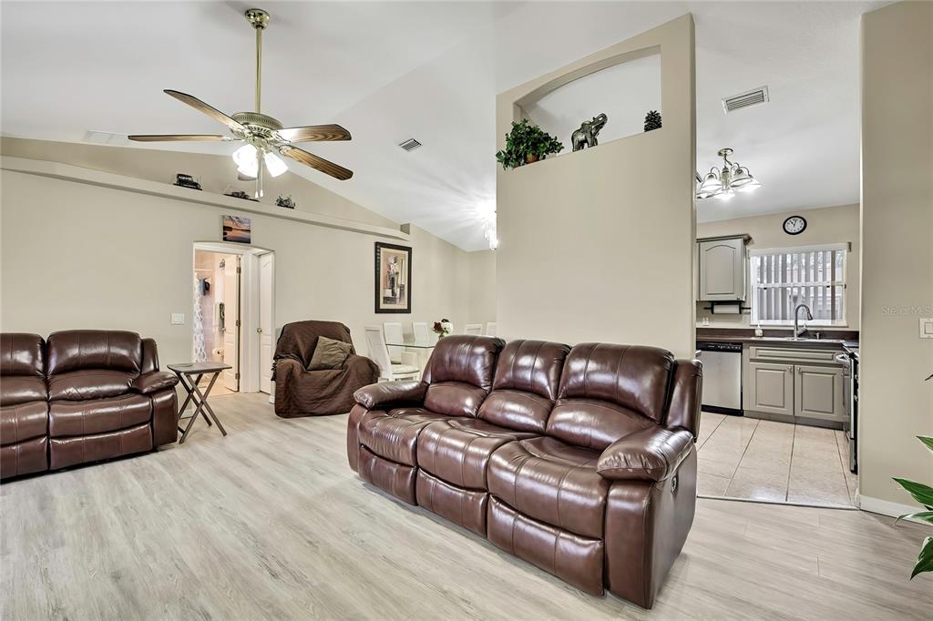 A living room with brown leather sofas, light wood-look flooring, and an open kitchen area — 103 DAISY LANE, INVERNESS, FL