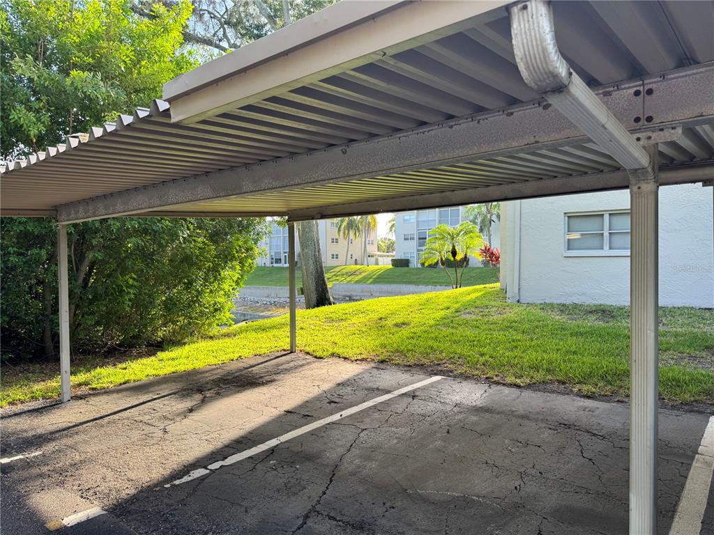 A covered parking carport with a cracked asphalt surface sits beside a grassy lawn — 946 VIRGINIA STREET UNIT 104, DUNEDIN, FL