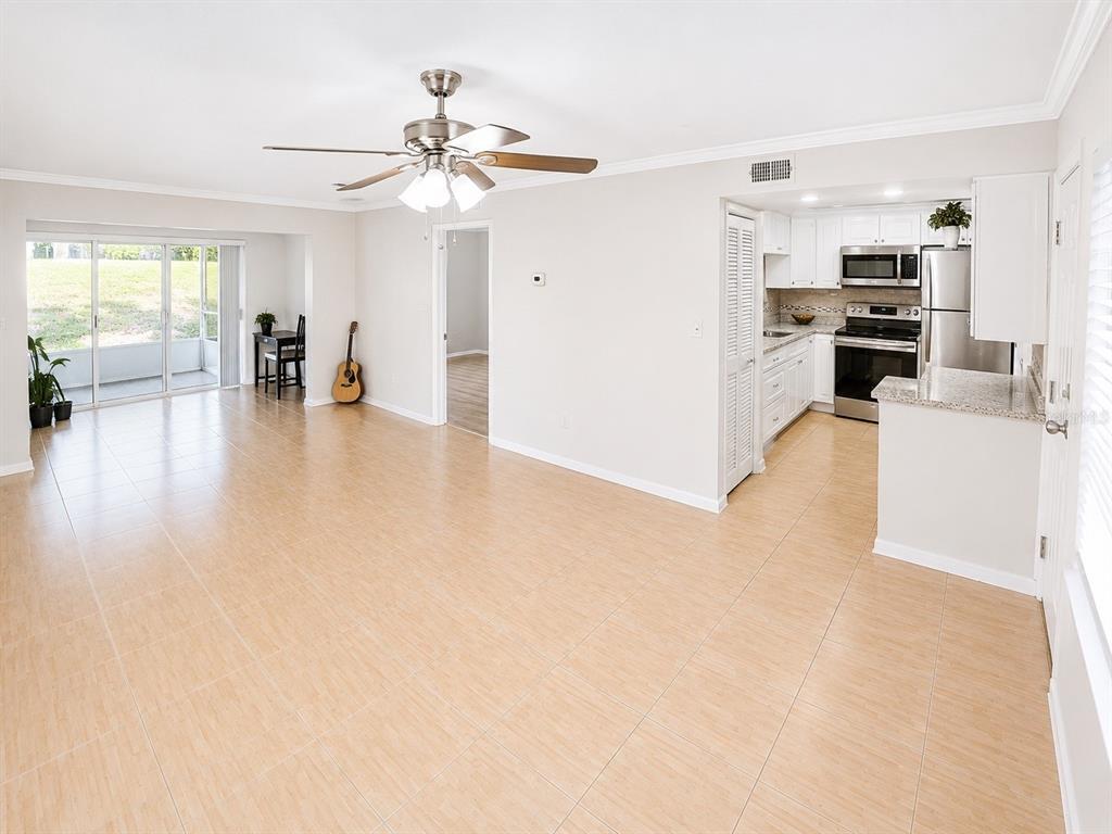 An open-concept living and dining area features light tile flooring, a ceiling fan, and kitchen — 946 VIRGINIA STREET UNIT 104, DUNEDIN, FL