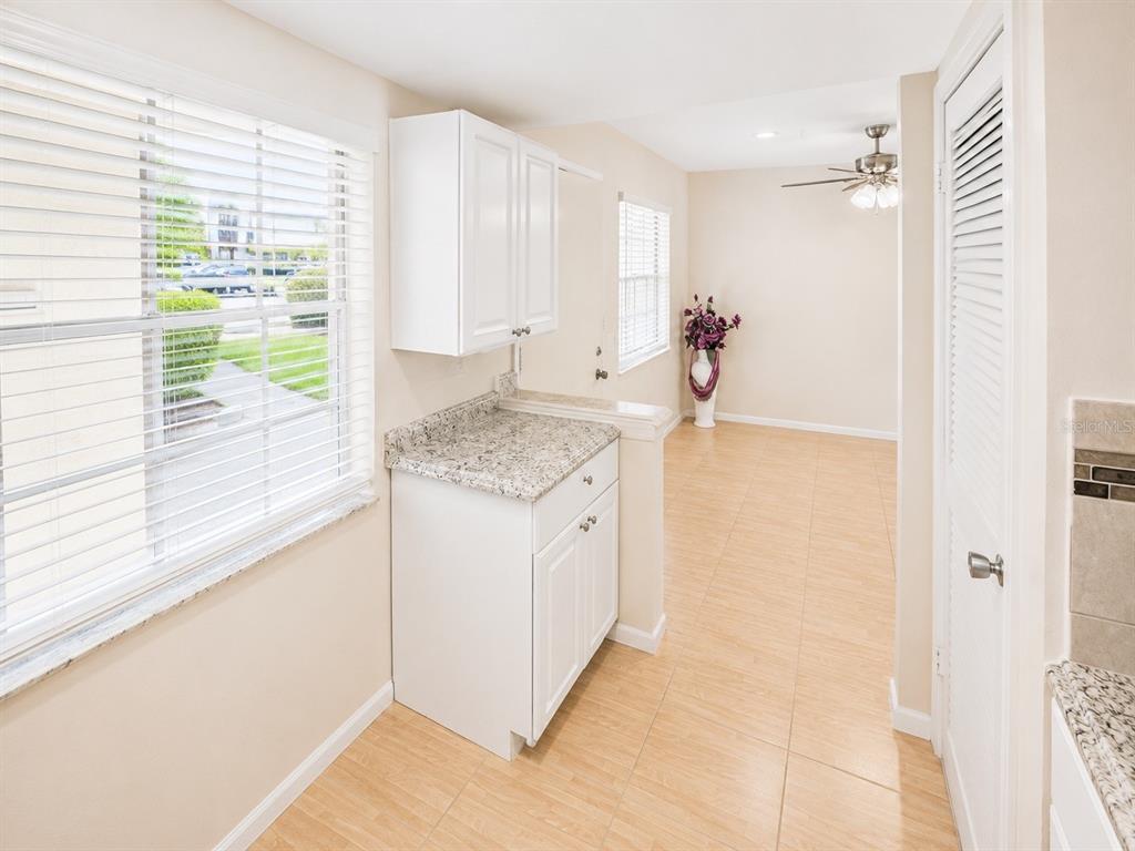 A kitchen area features white cabinets, granite countertops, tile flooring, and a view of outdoors — 946 VIRGINIA STREET UNIT 104, DUNEDIN, FL