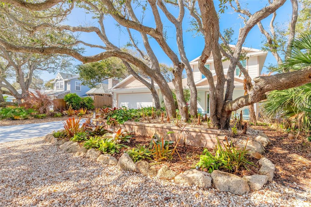 A house exterior features a stone retaining wall, tropical landscaping, and large trees in front — 68 GLENVIEW AVENUE, PONCE INLET, FL