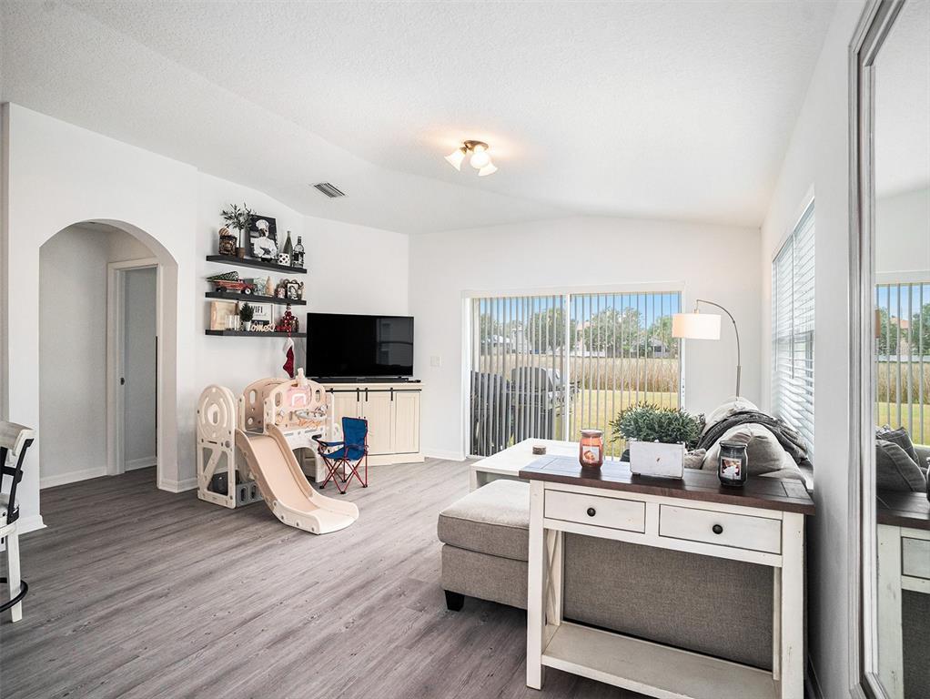 A living room features gray wood-look flooring, a sliding glass door, and a children's slide — 7833 CARRIAGE POINTE DRIVE, GIBSONTON, FL