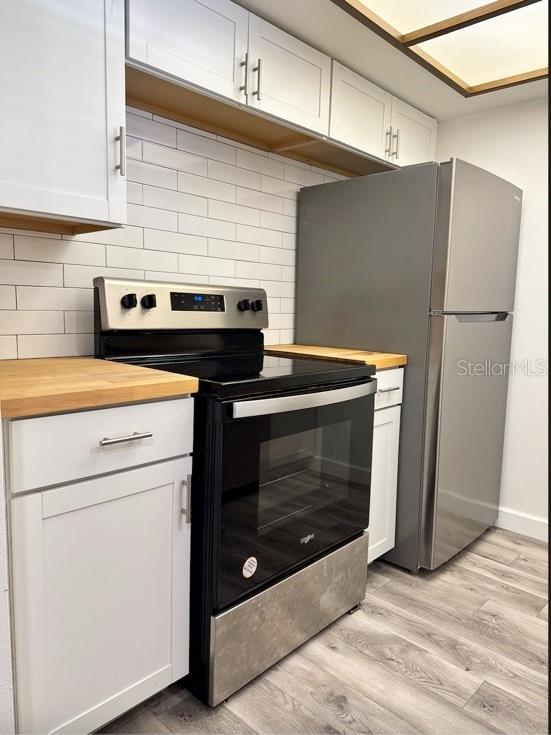 A kitchen features white cabinets, butcher block countertops, a stainless steel stove, and subway tile — 9700 STARKEY ROAD UNIT 322, SEMINOLE, FL