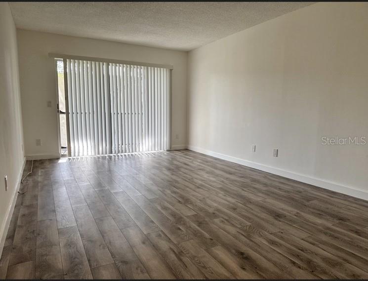 An empty living room features light wood-look flooring, white walls, and a sliding glass door — 9700 STARKEY ROAD UNIT 322, SEMINOLE, FL