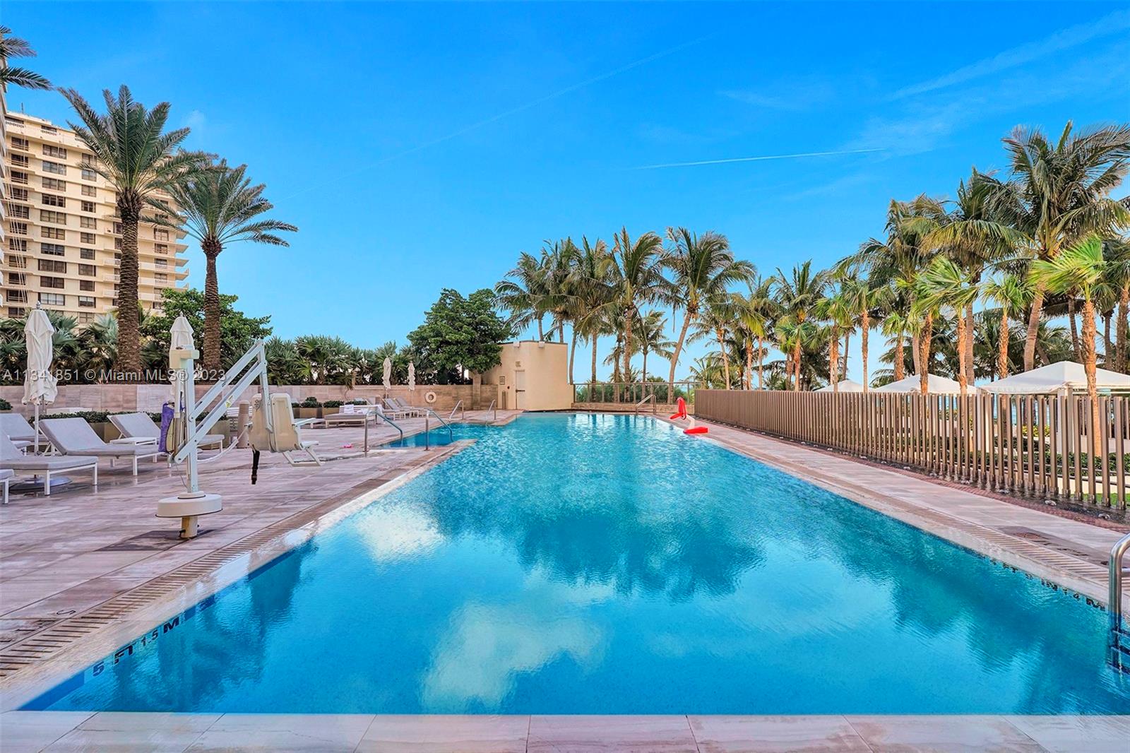 An outdoor swimming pool surrounded by palm trees and lounge chairs next to a building — 9703 Collins Ave # 2501, Bal Harbour FL 33154, BAL HARBOUR, FL