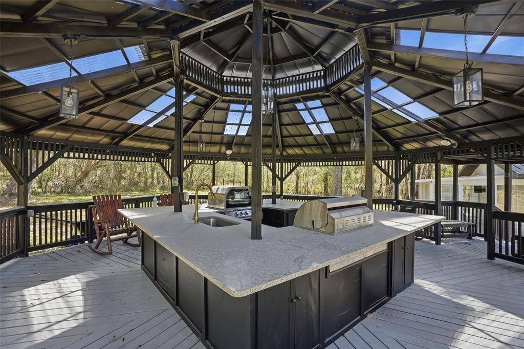 An outdoor kitchen with a granite countertop and grill sits under a large wooden gazebo — 15458 SNOW MEMORIAL HIGHWAY, BROOKSVILLE, FL