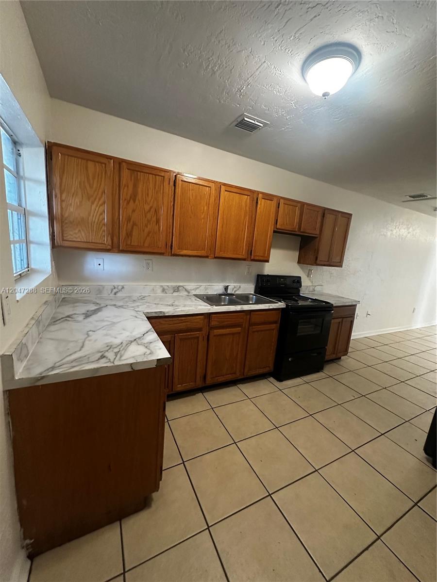 A kitchen features wood cabinets, marble-patterned laminate countertops, a black stove, and tiled floors — MIAMI, FL