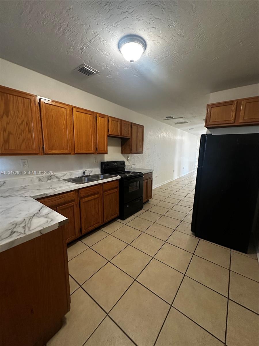A kitchen features oak cabinets, white marble-patterned countertops, black appliances, and light-colored floor tiles — MIAMI, FL