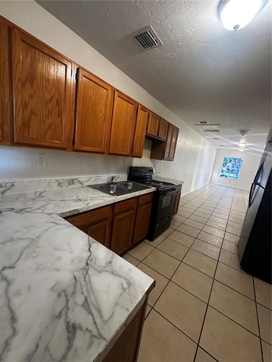 A kitchen features oak cabinets, marble-patterned laminate countertops, and black appliances over tiled floors — MIAMI, FL