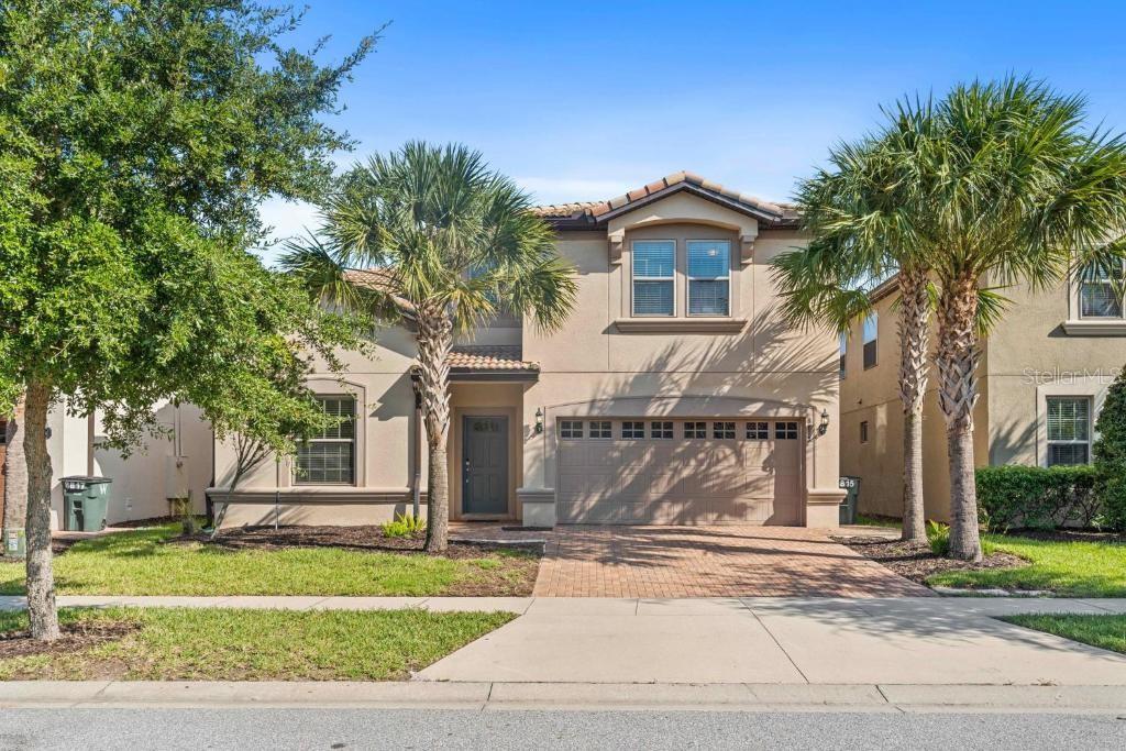 A two-story suburban house with a tan stucco exterior, a two-car garage, and palm trees — 8815 MACAPA DRIVE, KISSIMMEE, FL