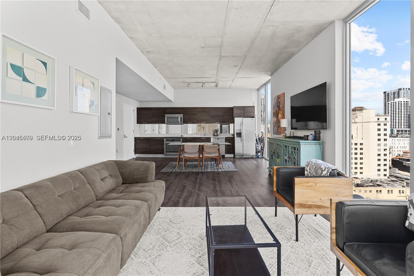 A modern open-concept living room and kitchen feature concrete ceilings, dark cabinetry, and city views — 151 SE 1st St # 1402, Miami FL 33131, MIAMI, FL