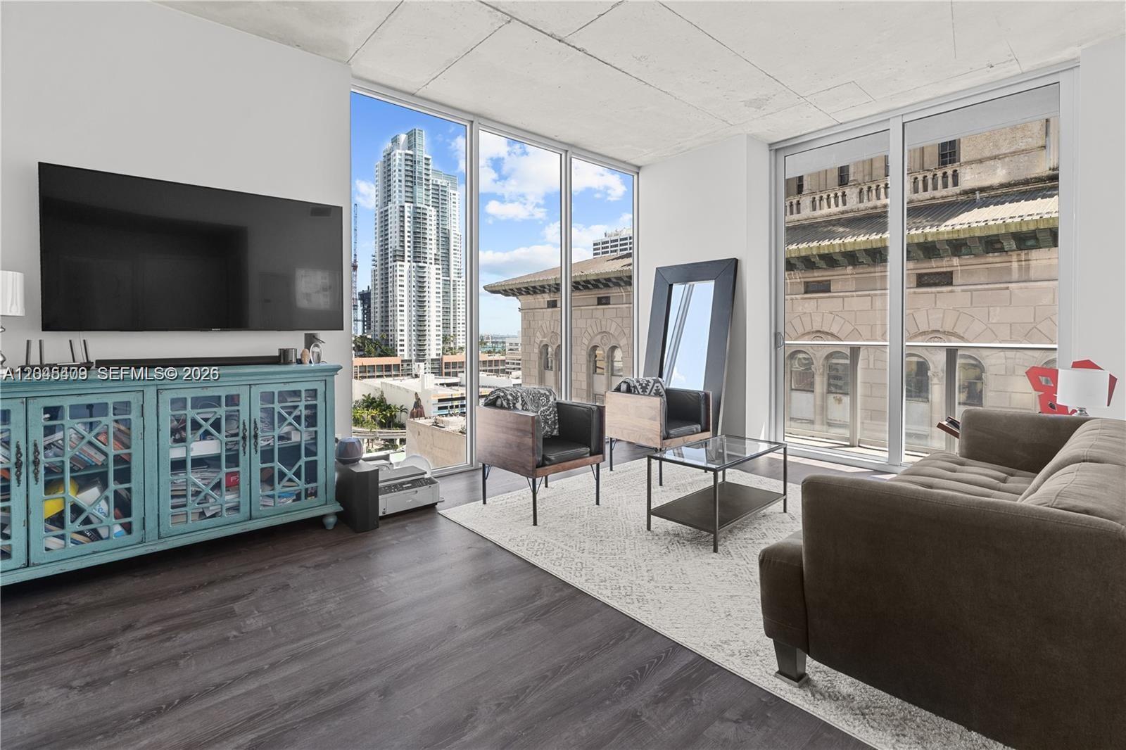 A modern living room features floor-to-ceiling windows, dark wood flooring, and a view of skyscrapers — 151 SE 1st St # 1402, Miami FL 33131, MIAMI, FL