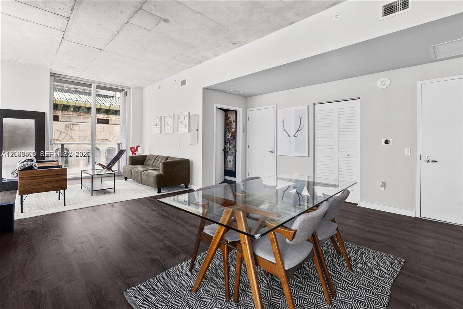 A modern open-concept living and dining area features concrete ceilings, dark wood floors, and floor-to-ceiling windows — 151 SE 1st St # 1402, Miami FL 33131, MIAMI, FL
