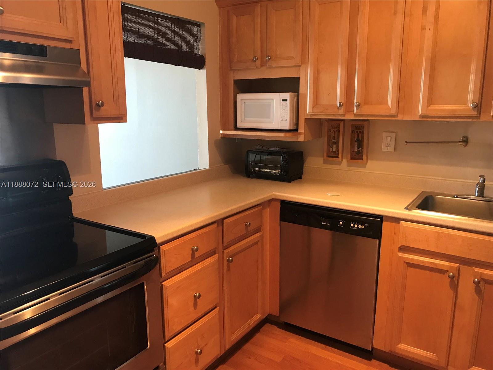 A kitchen features light wood cabinets, stainless steel appliances, and a beige countertop — 1000 Parkview Dr # 627, Hallandale Beach FL 33009, HALLANDALE BEACH, FL
