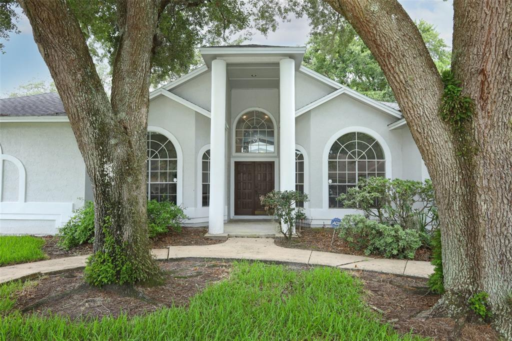 A single-story house with a columned entryway, arched windows, and large trees in the yard — 2357 CHANTILLY TERRACE, OVIEDO, FL