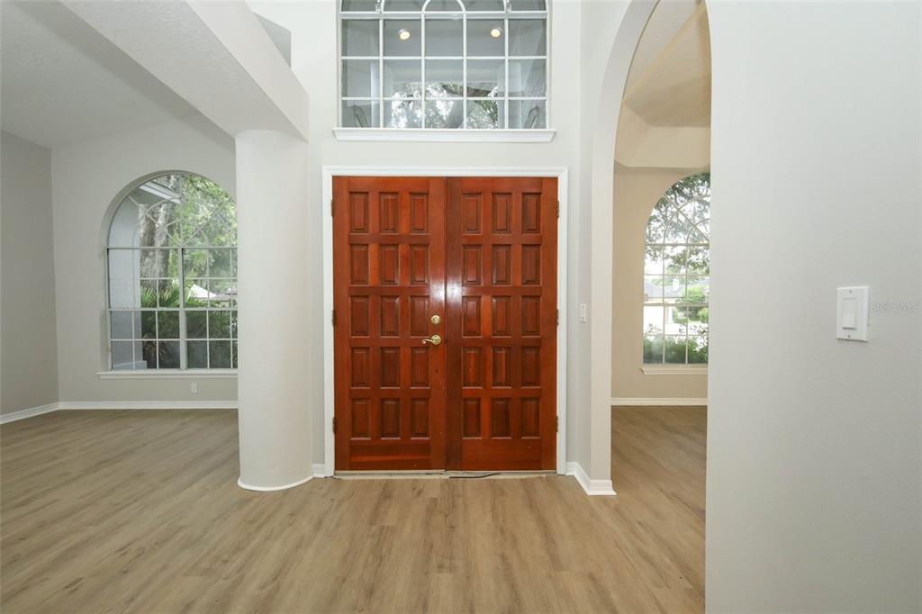 A foyer with light wood-look flooring, double wooden front doors, and arched windows — 2357 CHANTILLY TERRACE, OVIEDO, FL