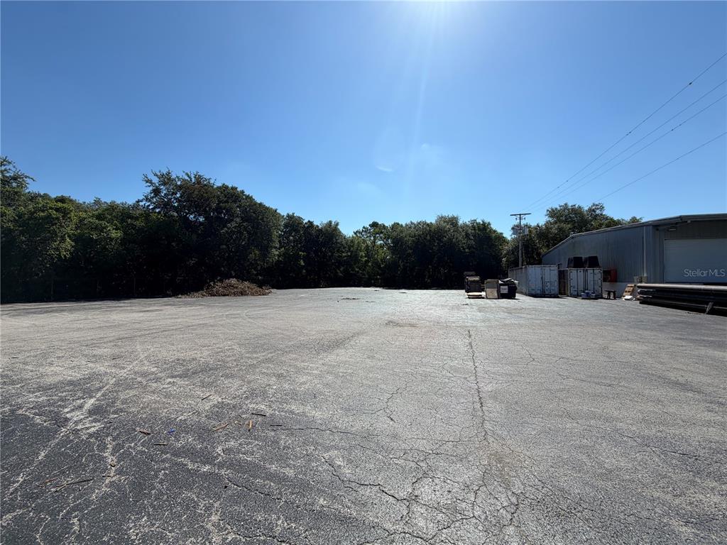 A large, paved outdoor lot sits adjacent to a metal warehouse building and wooded area — 510 N TURKEY CREEK ROAD, PLANT CITY, FL