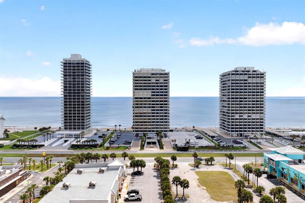 Three tall residential towers stand along a beach with a parking lot in the foreground — 2900 N ATLANTIC AVENUE UNIT 1006, DAYTONA BEACH, FL