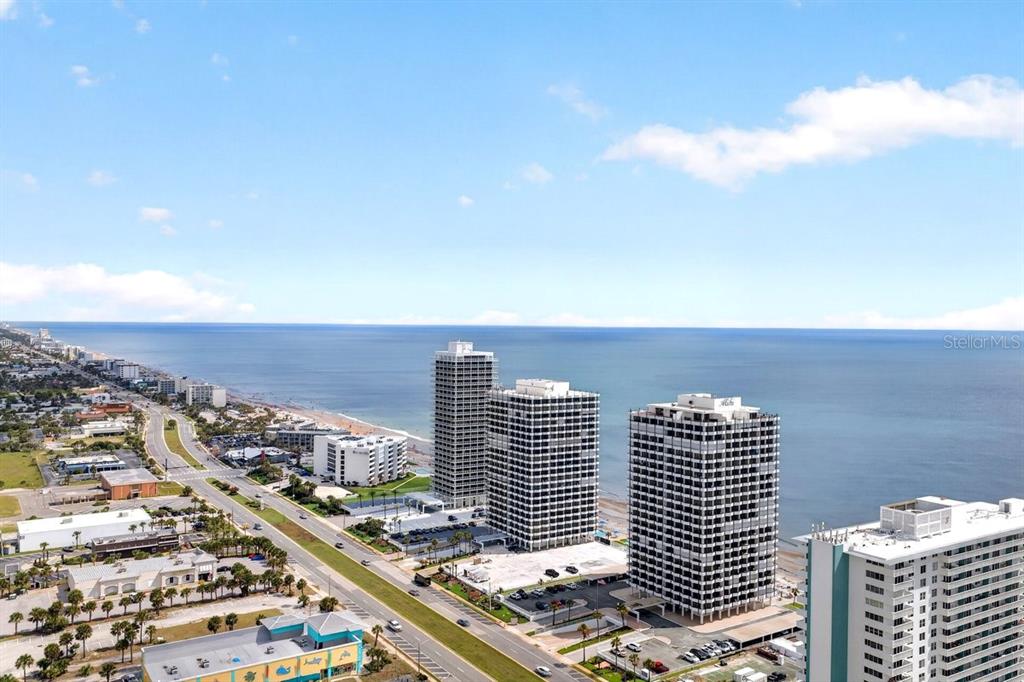 An aerial view shows several high-rise buildings along a coastline next to a highway — 2900 N ATLANTIC AVENUE UNIT 1006, DAYTONA BEACH, FL