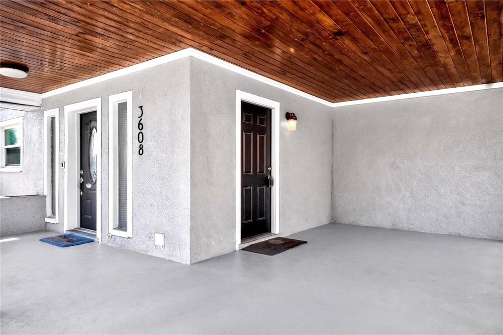 A covered porch features a wood-paneled ceiling, gray concrete flooring, and two dark entry doors — 3608 W CARMEN STREET, TAMPA, FL