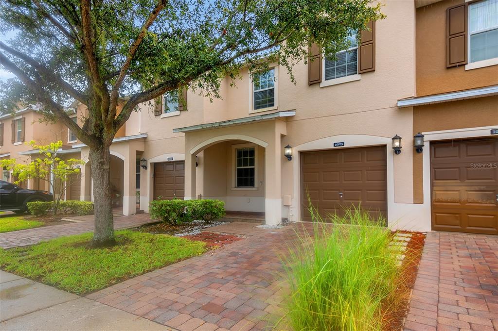 A two-story townhouse exterior with a brick paver driveway, brown garage doors, and a tree — 10975 SAVANNAH LANDING CIRCLE, ORLANDO, FL