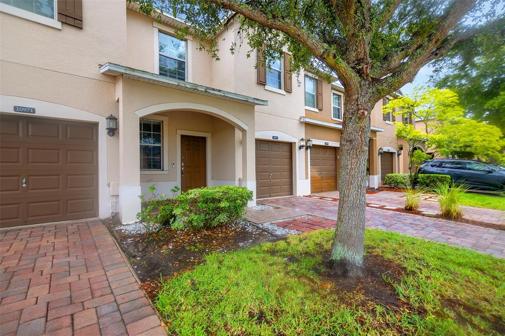 A row of tan townhouses with brown garage doors and a large tree in front — 10975 SAVANNAH LANDING CIRCLE, ORLANDO, FL