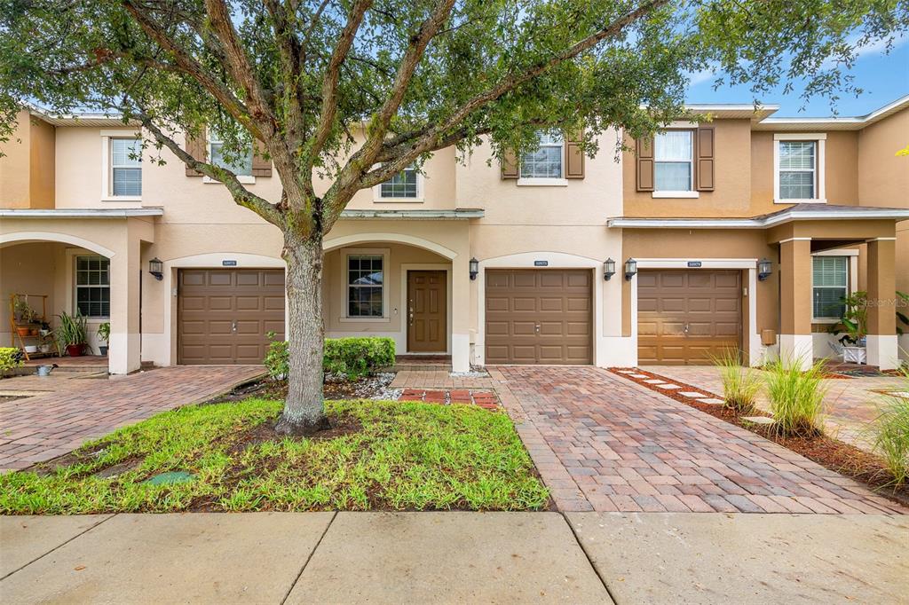 A row of three townhouses with brown garage doors, tan stucco walls, and paved driveways — 10975 SAVANNAH LANDING CIRCLE, ORLANDO, FL