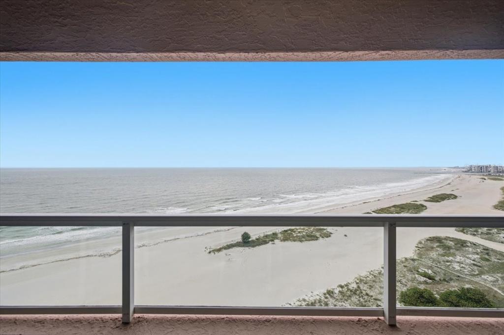 A balcony view overlooking a sandy beach and the ocean under a clear blue sky — 1310 GULF BOULEVARD UNIT 18C, CLEARWATER, FL