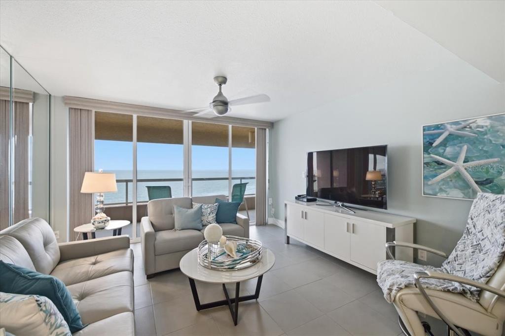 A living room features light gray sofas, a white media console, and a balcony overlooking water — 1310 GULF BOULEVARD UNIT 18C, CLEARWATER, FL