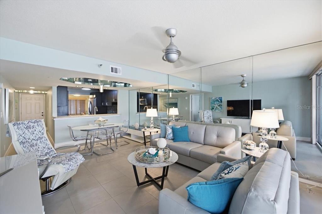 A living room features light gray sofas, a round coffee table, and a mirrored wall — 1310 GULF BOULEVARD UNIT 18C, CLEARWATER, FL