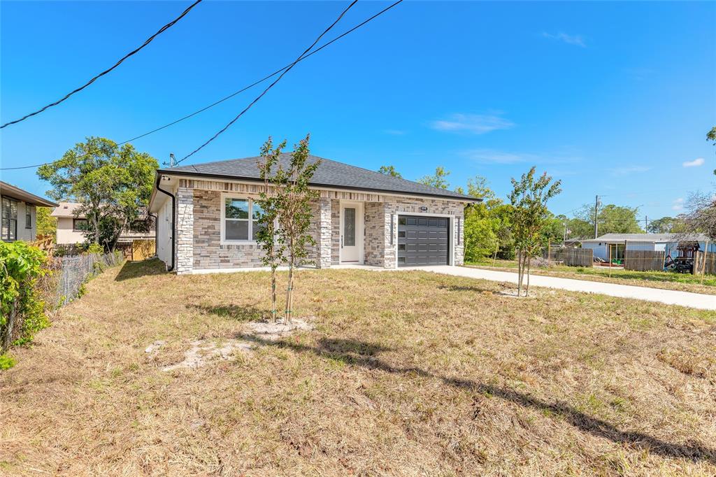 A single-story house with a stone facade, a dark garage door, and a concrete driveway — 1991 CEDAR STREET, DAYTONA BEACH, FL
