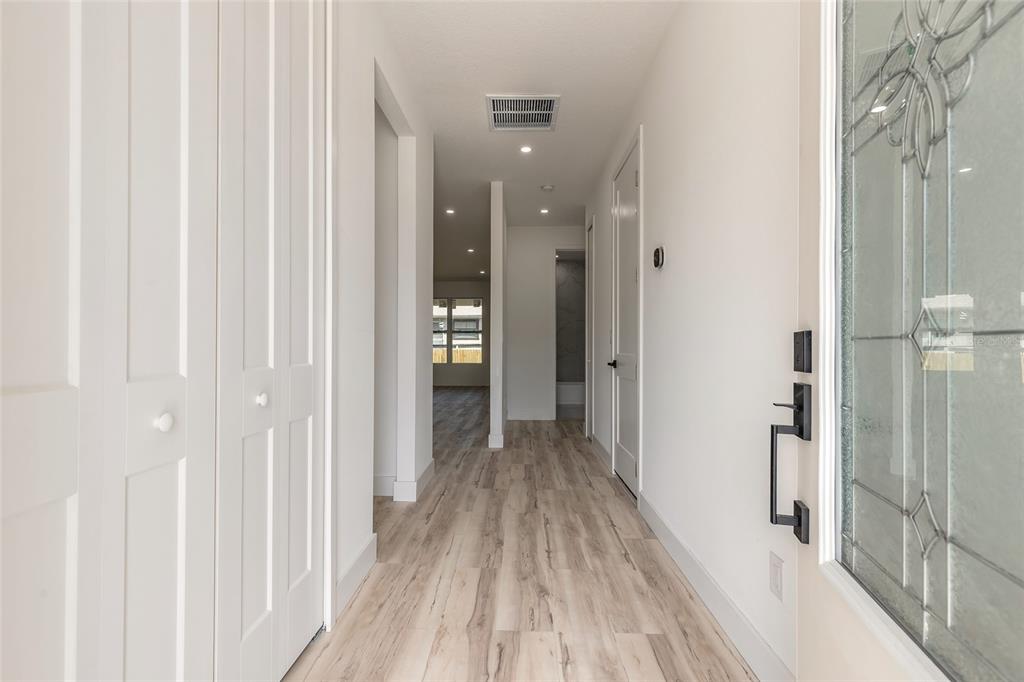 A bright hallway features light wood-look flooring, white walls, and a glass-paneled front door — 1991 CEDAR STREET, DAYTONA BEACH, FL