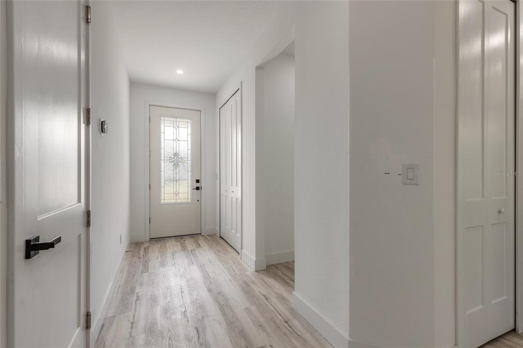 A bright entryway features light wood-look flooring, white walls, and a glass-paneled front door — 1991 CEDAR STREET, DAYTONA BEACH, FL
