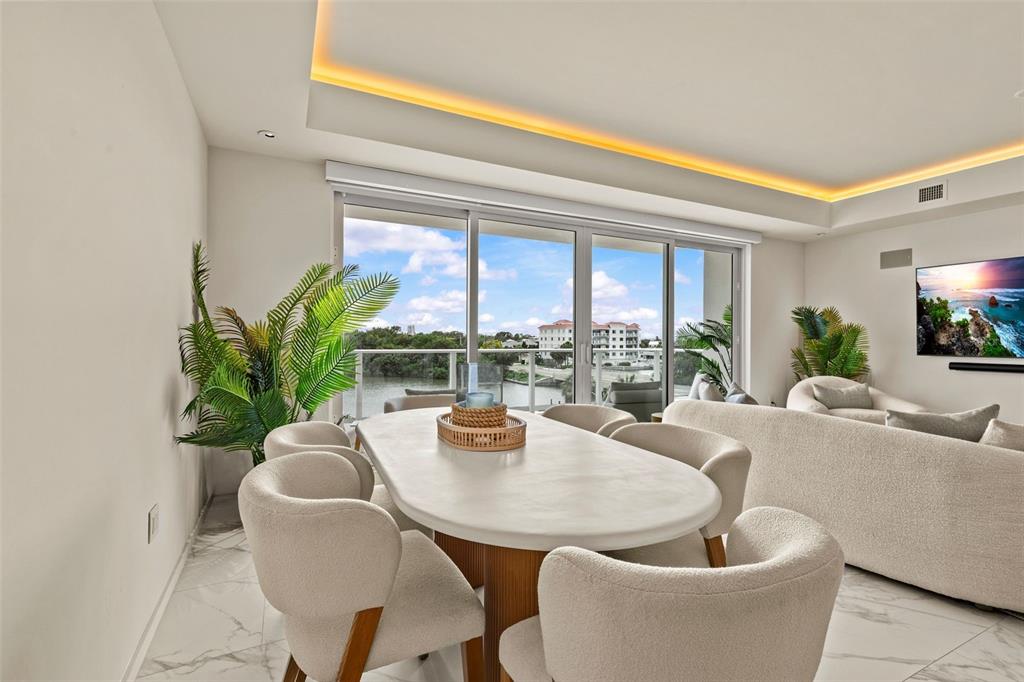 A dining area with a white oval table and chairs overlooks a balcony and water — 1020 SUNSET POINT ROAD UNIT 310, CLEARWATER, FL