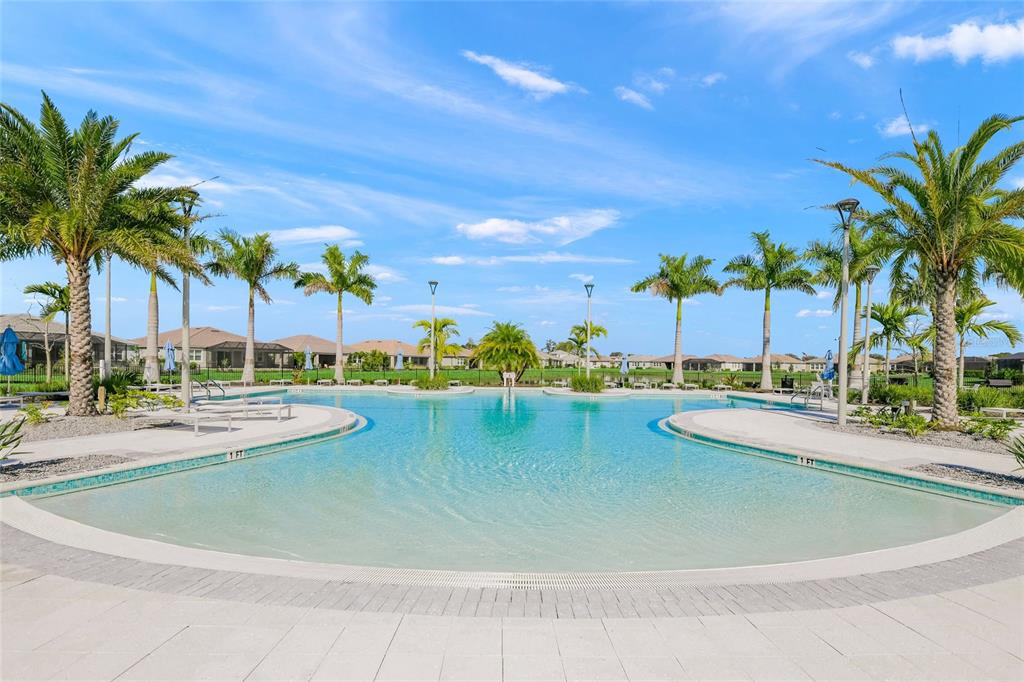 A resort-style swimming pool with a zero-entry edge is surrounded by palm trees and houses — 8681 RAIN SONG ROAD, SARASOTA, FL