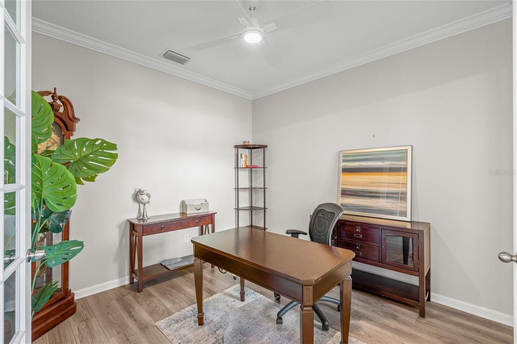 A home office features a wooden desk, a tall bookshelf, and a large potted plant — 8681 RAIN SONG ROAD, SARASOTA, FL
