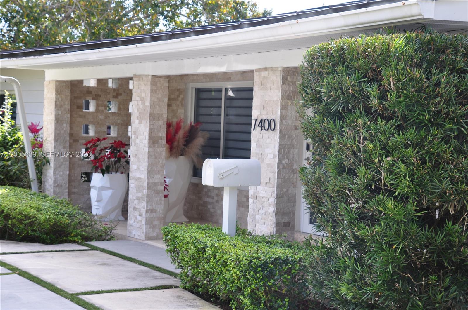 A stone-clad exterior features a covered porch, decorative planters, and a white mailbox — 7400 SW 116th St, Pinecrest FL 33156, PINECREST, FL