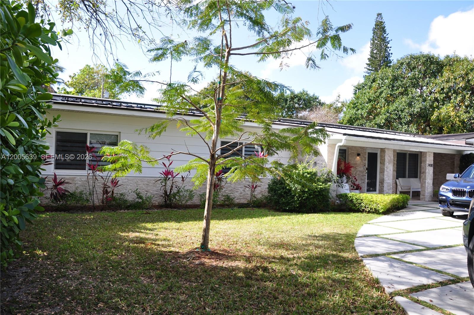 A single-story house with white siding, stone accents, and a circular concrete driveway — 7400 SW 116th St, Pinecrest FL 33156, PINECREST, FL