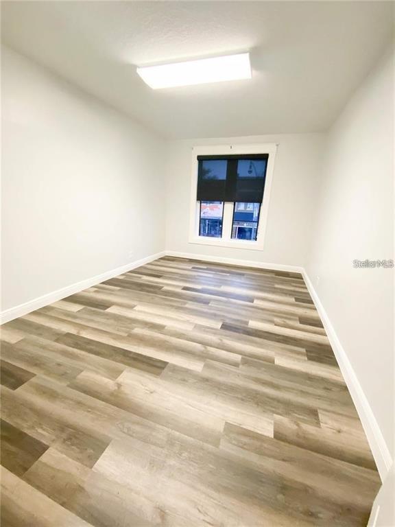 An empty room features light gray walls, wood-look plank flooring, and a single window — 103 BROADWAY UNIT 204, KISSIMMEE, FL
