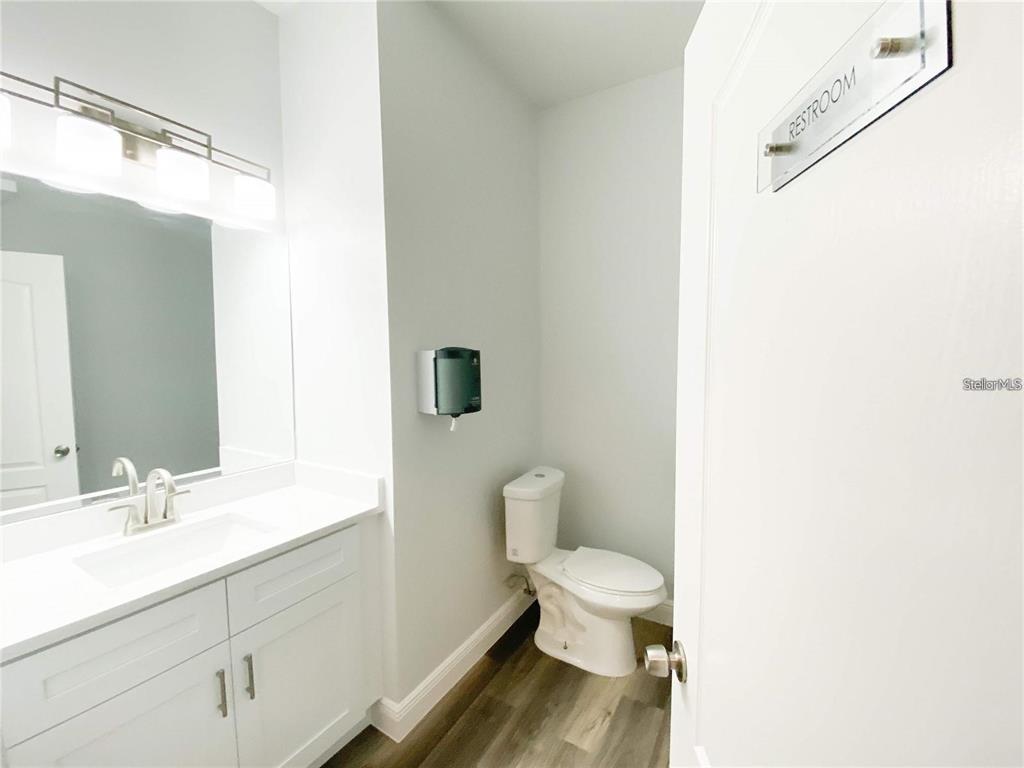 A modern bathroom features a white vanity, a toilet, and a wall-mounted soap dispenser — 103 BROADWAY UNIT 204, KISSIMMEE, FL