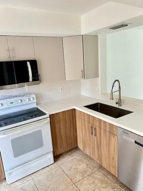 A kitchen features light-colored upper cabinets, wood-grain lower cabinets, a white stove, and a sink — 2355 SW 15th St # 73, Deerfield Beach FL 33442, DEERFIELD BEACH, FL