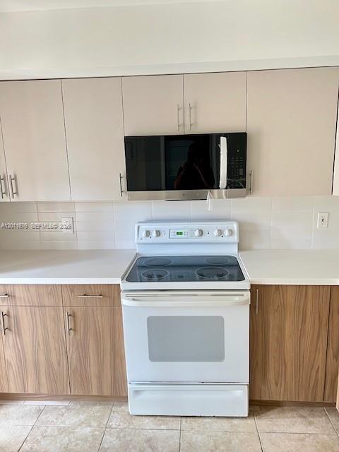 A kitchen features light wood cabinets, white countertops, a white electric stove, and a microwave — 2355 SW 15th St # 73, Deerfield Beach FL 33442, DEERFIELD BEACH, FL