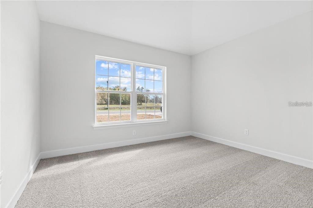 An empty bedroom features light gray walls, beige carpeting, and a window with exterior views — 4 SERIEMA COURT, PALM COAST, FL