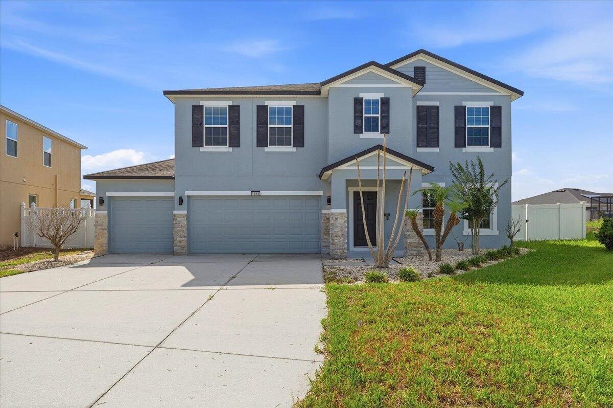 A two-story suburban house with a light blue exterior, stone accents, and a three-car garage — 9012 Orange Blossom Loop, FL 33844, FL
