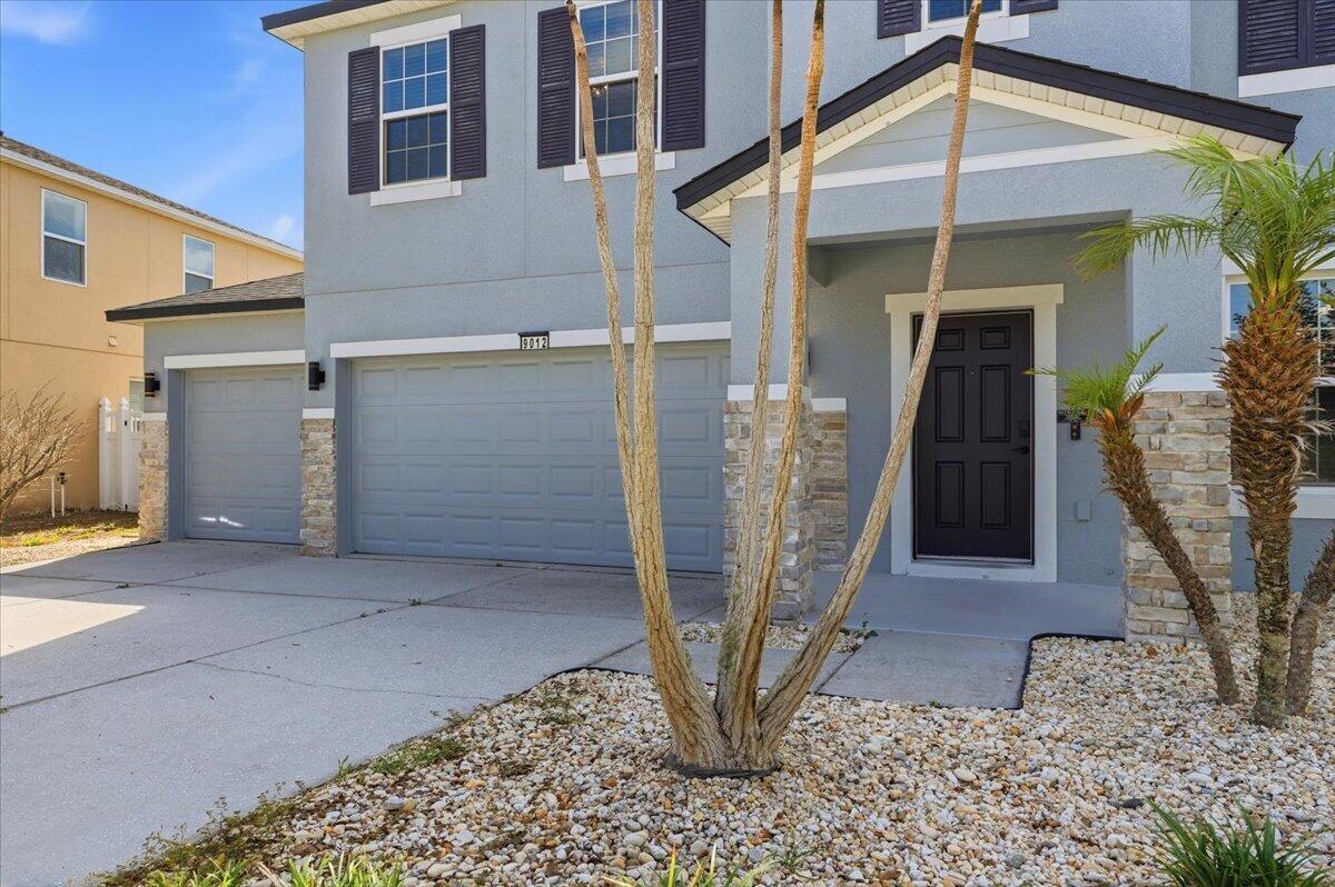A two-story house exterior features a gray facade, stone accents, and a three-car garage — 9012 Orange Blossom Loop, FL 33844, FL