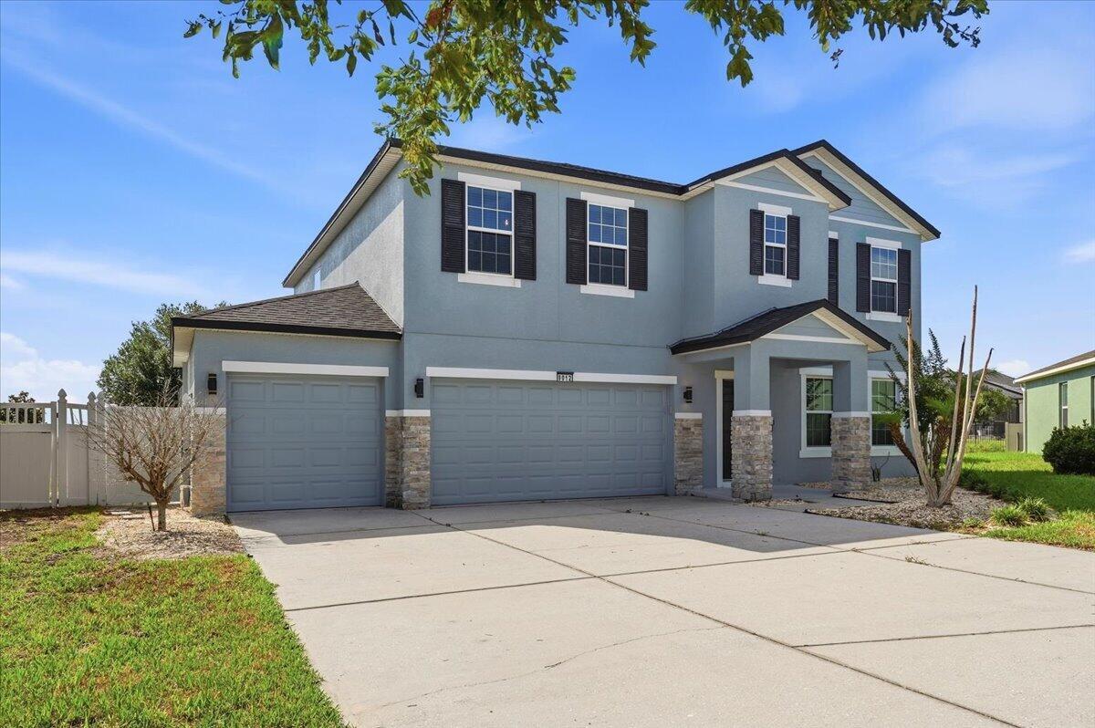 A two-story house with blue siding, stone accents, and a three-car garage — 9012 Orange Blossom Loop, FL 33844, FL