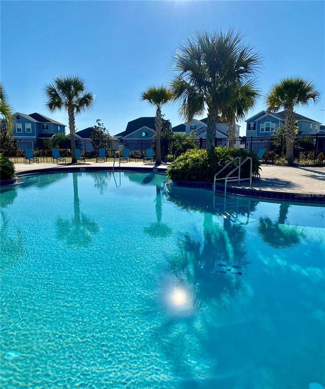 A swimming pool sits in front of palm trees and residential houses under a clear sky — 2921 SENTENCE STREET, KISSIMMEE, FL