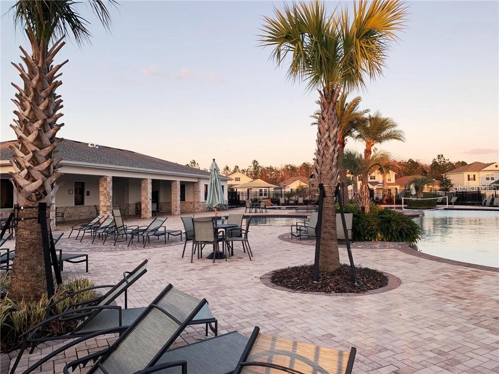 A paved pool deck features lounge chairs, dining tables, palm trees, and a covered patio area — 2921 SENTENCE STREET, KISSIMMEE, FL