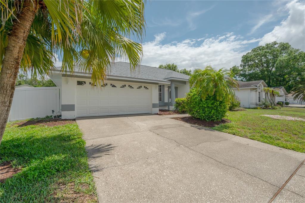 A single-story house with a white garage, gray roof, and a front yard with palms — 15121 HEATHRIDGE DRIVE, TAMPA, FL